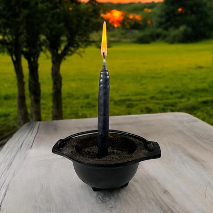 Neatos Elements hand-dipped black candle in a cauldron holder, lit outdoors at sunset.