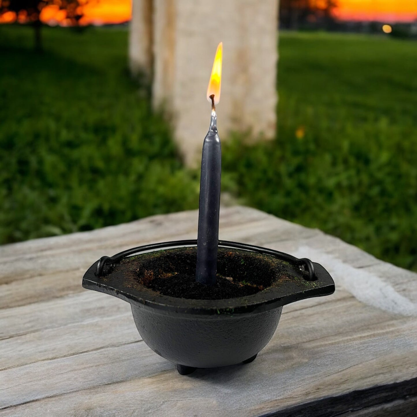 Neatos Elements hand-dipped black chime candle in a cauldron, lit outdoors at sunset.