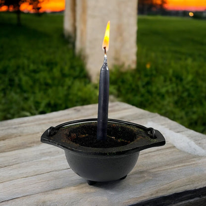 Neatos Elements hand-dipped black chime candle in a cauldron, lit outdoors at sunset.