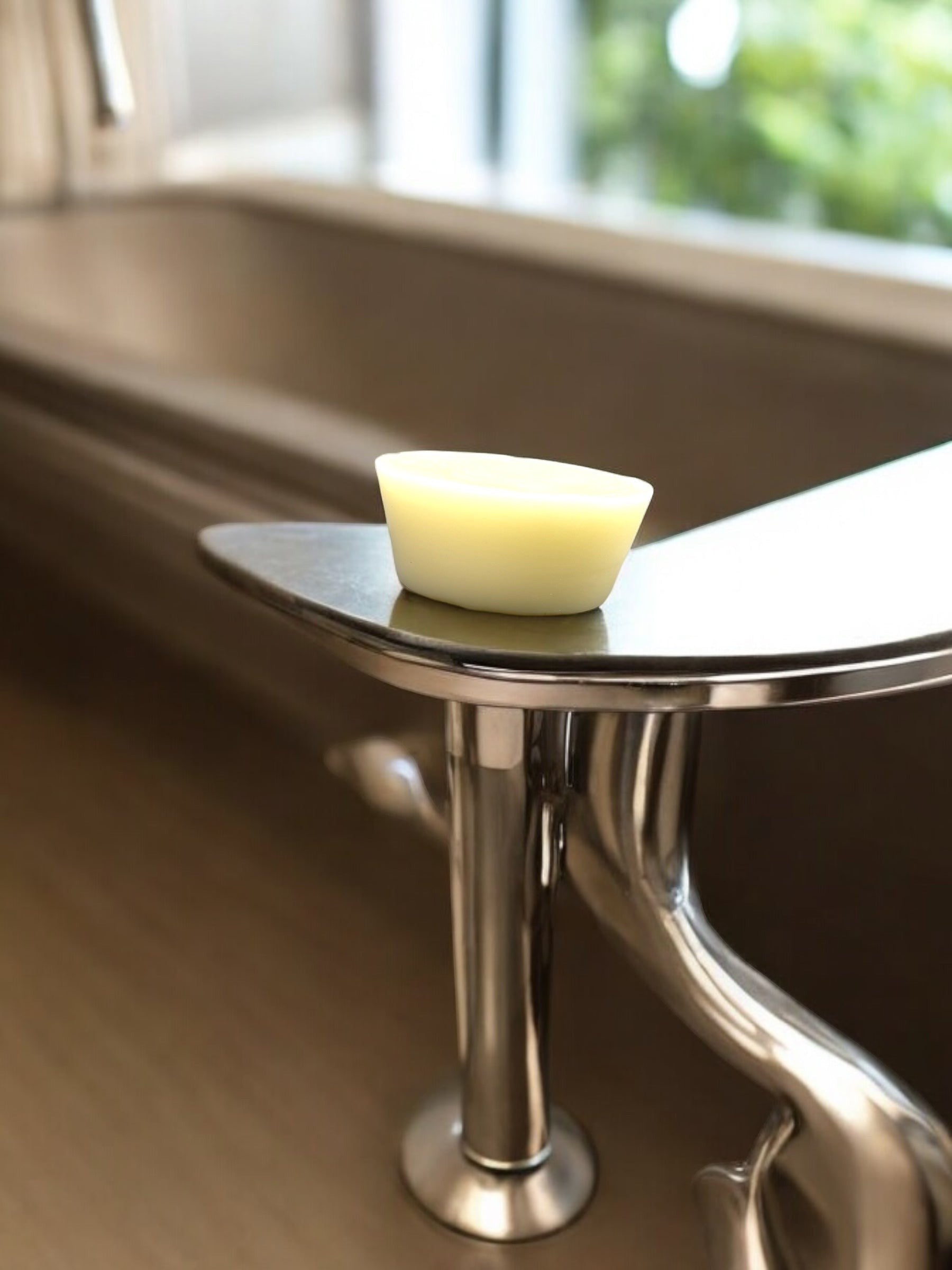 Neatos Elements Blitz Lotion Bar, a pale yellow solid bar with a curved top, resting on a metallic shelf next to a bathtub.