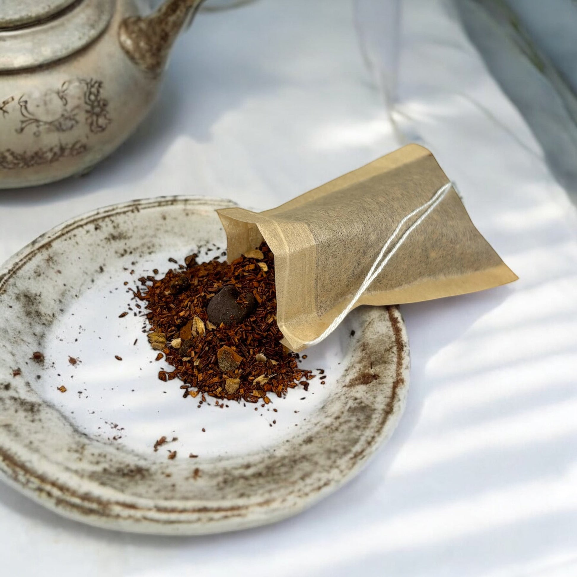 Neatos Elements Choco Chai Tea Blend loose leaf tea with chocolate chips and spices in a tea bag on a rustic plate.