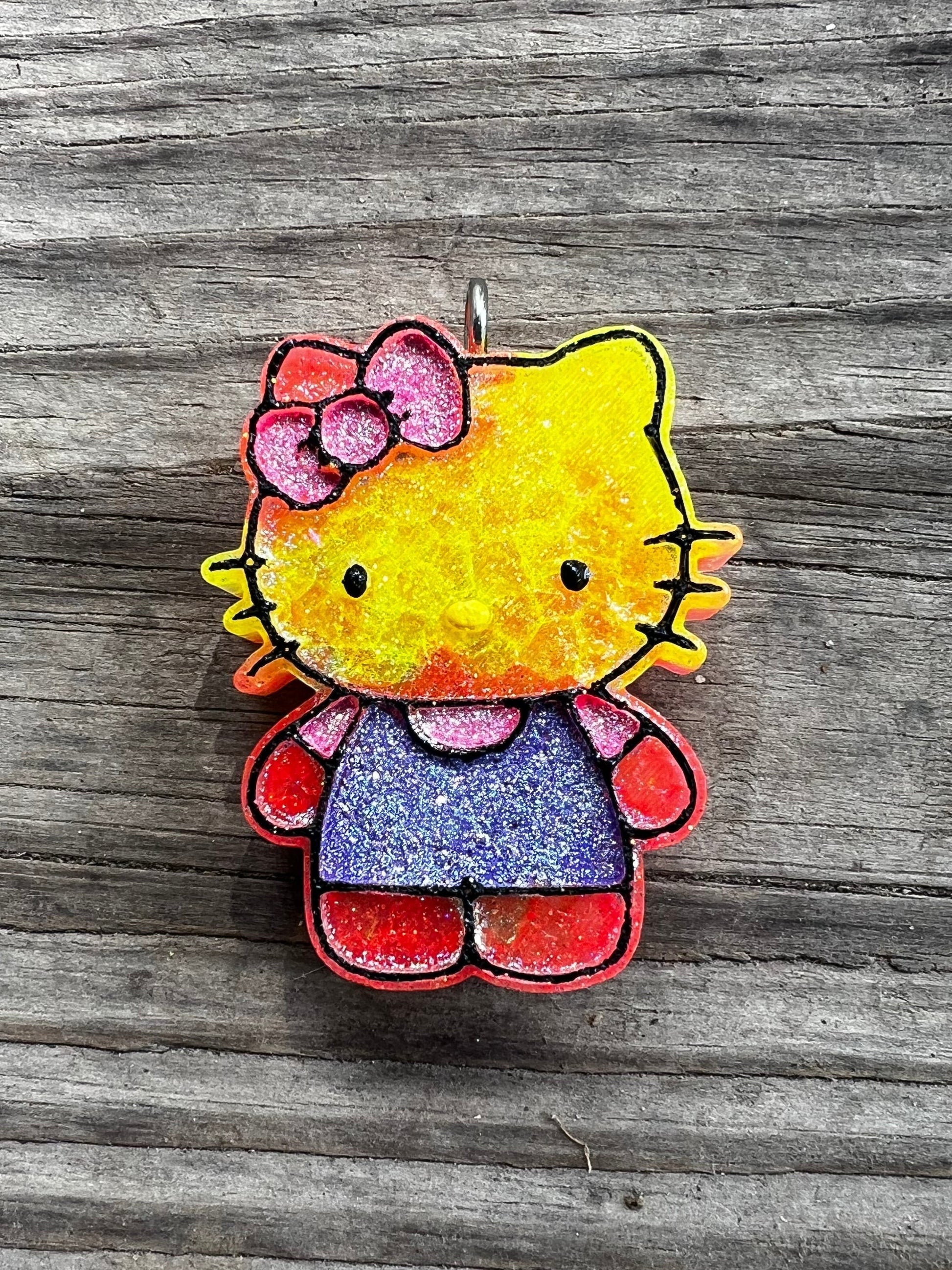 Neatos Elements Island Sunset Hello Kitty car freshie with yellow head, pink bow, blue dress, and red legs.