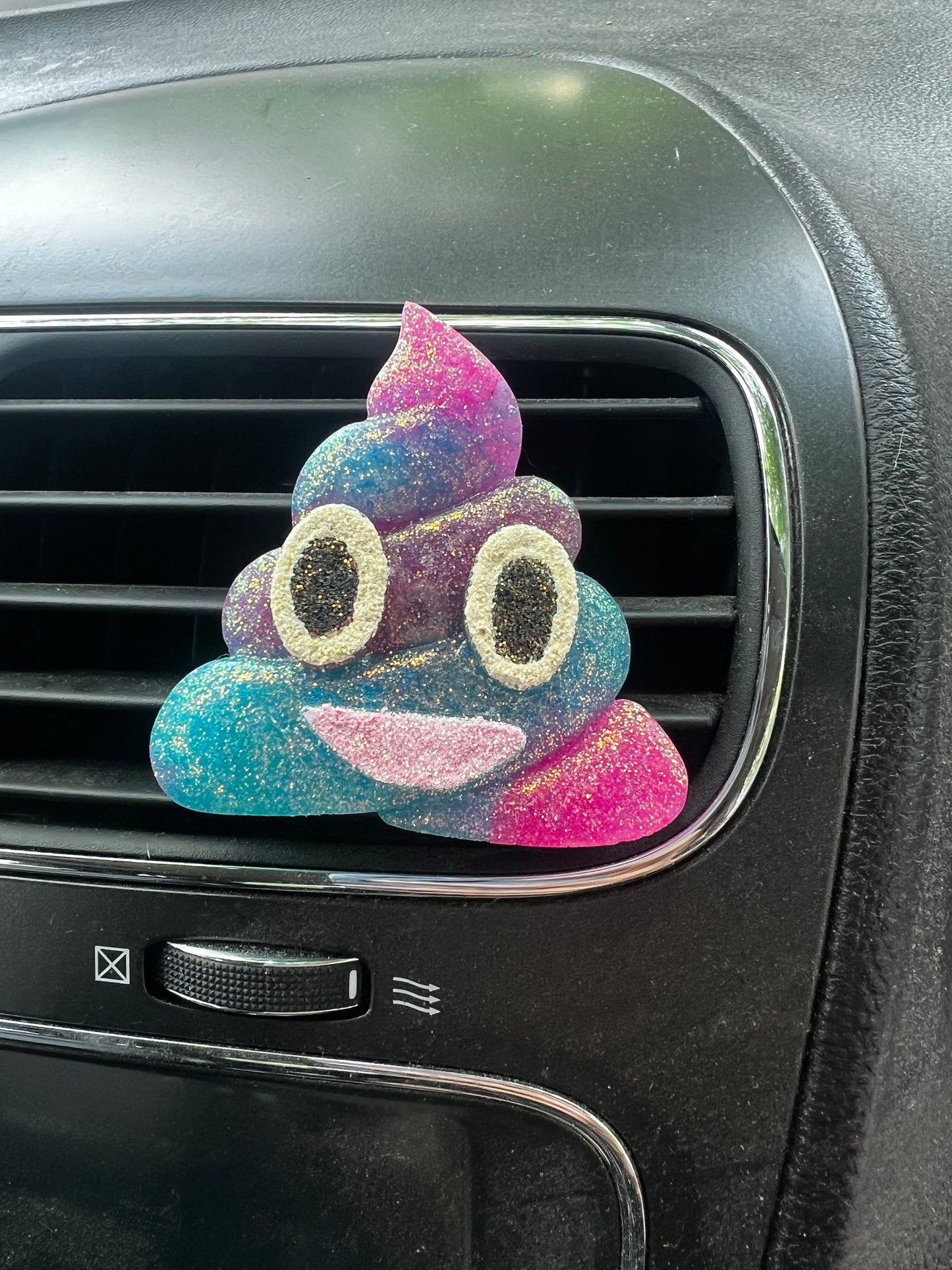 Neatos Elements glittery poop emoji car vent freshie in pink, blue, and purple with googly eyes and a smiling mouth.