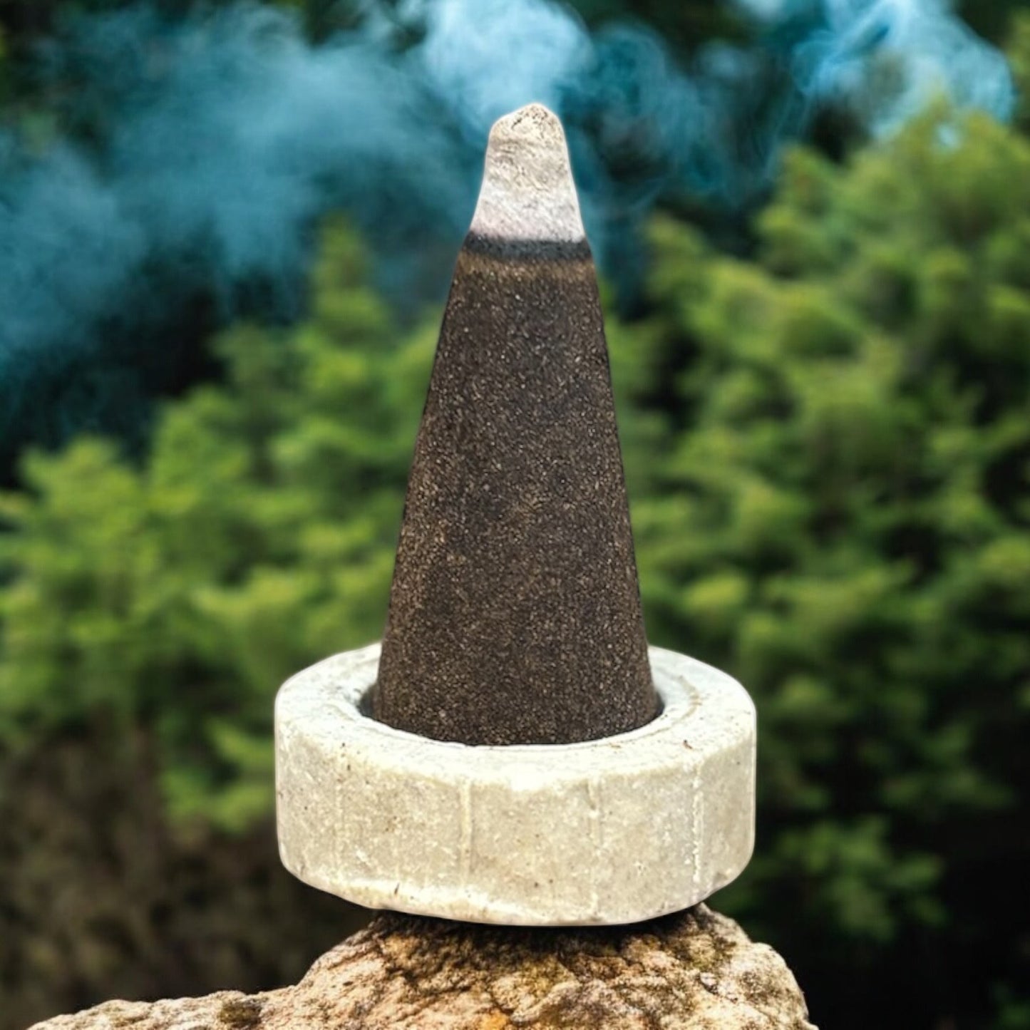 Neatos Elements Tree of Life incense cone burning with blue smoke, set in a stone holder outdoors.