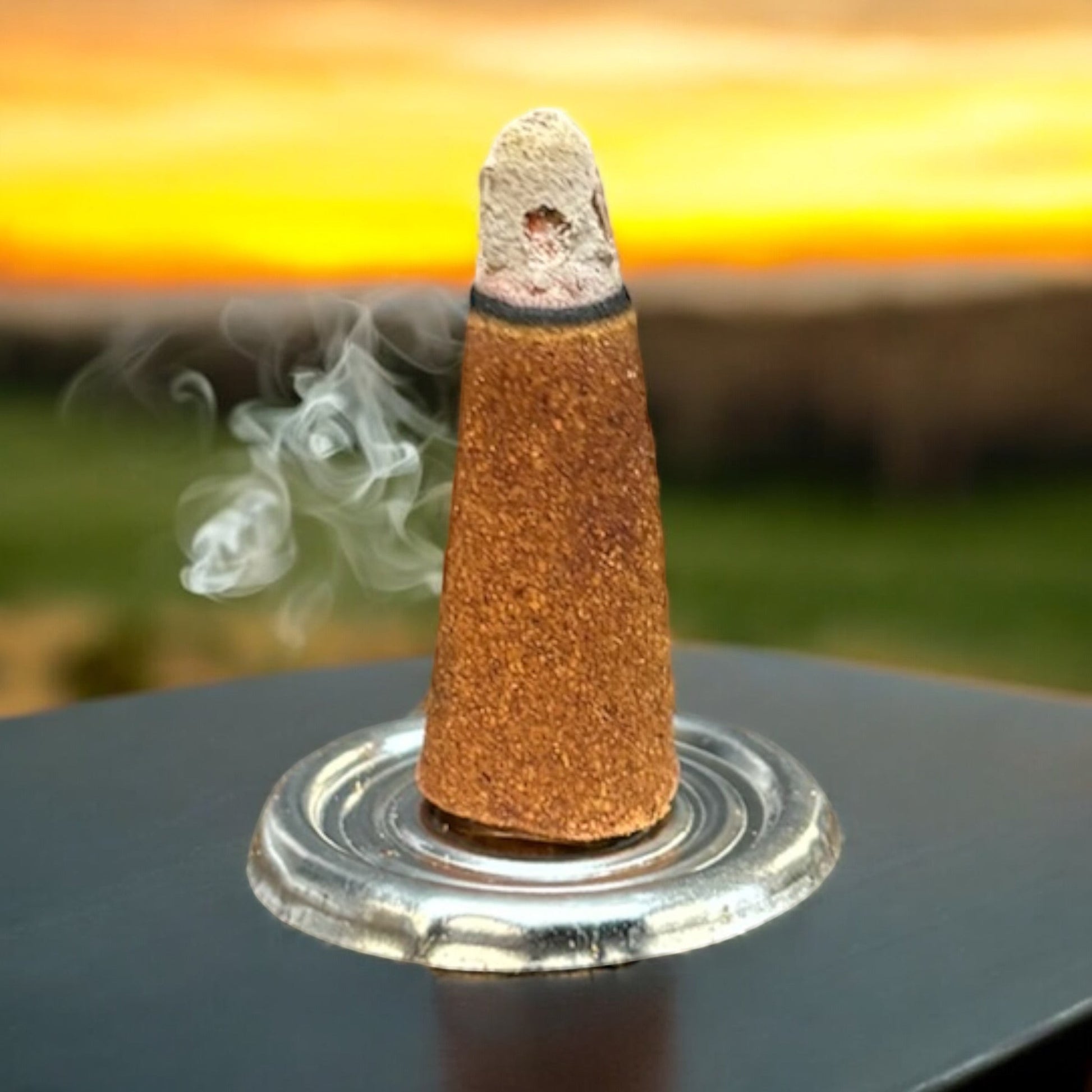 Neatos Elements White Sage Incense Cone burning with smoke, set against a sunset backdrop.