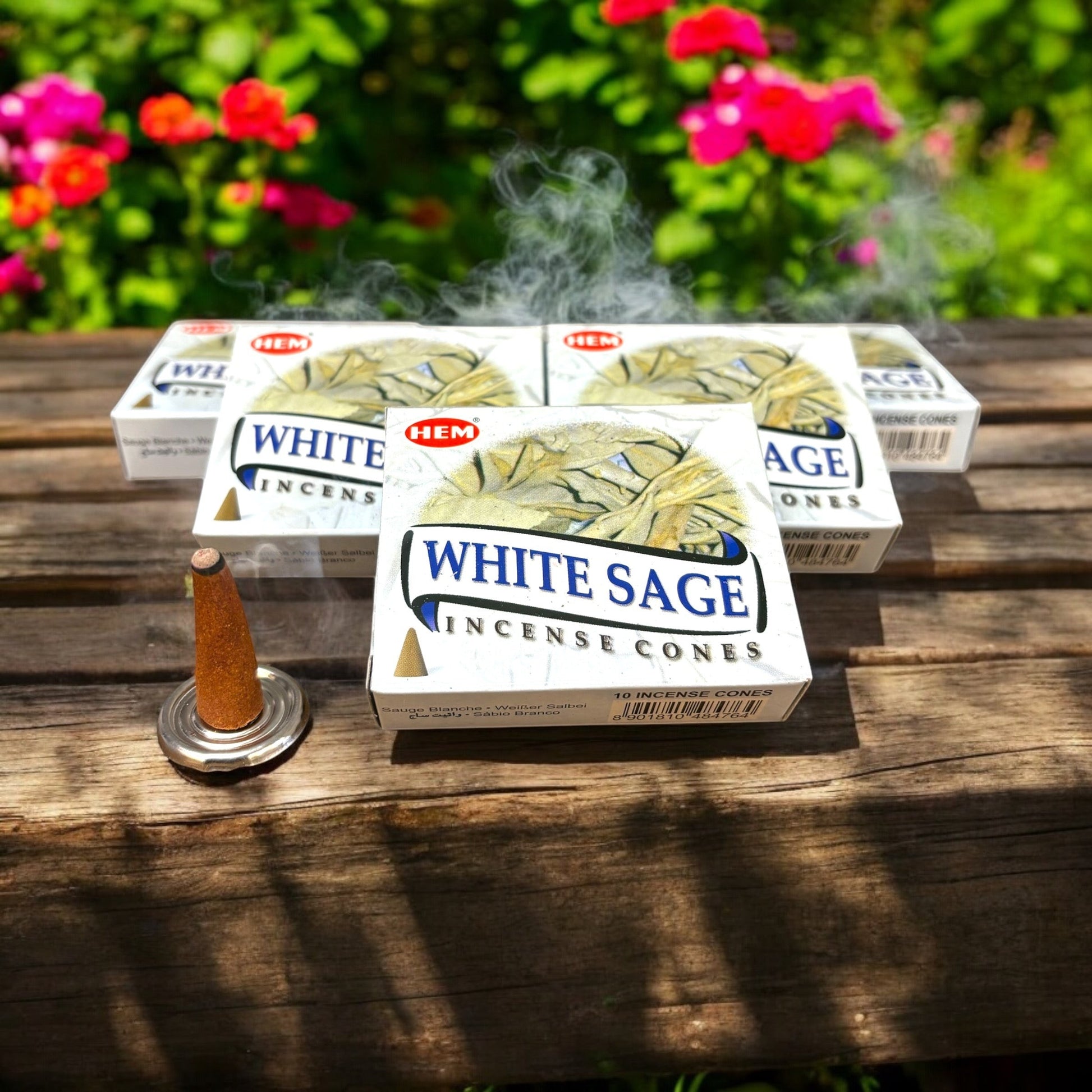 Neatos Elements White Sage incense cones burning, releasing smoke, on a wooden table with floral background.