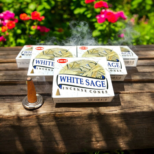 Neatos Elements White Sage incense cones burning, releasing smoke, on a wooden table with floral background.